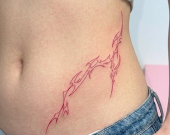 May include: A red ink tattoo design featuring sharp, elongated, and jagged lines that follow a flowing, organic path across the skin. The tattoo consists of thin, continuous outlines that create a series of interconnected, pointed shapes.