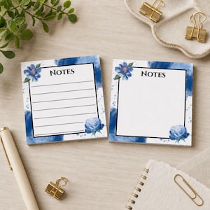 May include: Two square sticky note pads featuring a white centre with a black border and the word NOTES printed at the top. The background has a blue watercolour wash with blue floral illustrations in the corners. One pad is lined, one is blank.