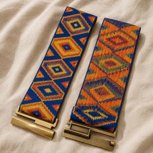 Puede incluir: Dos cinturones el&aacute;sticos con patrones geom&eacute;tricos en azul, naranja y amarillo. Cada cintur&oacute;n tiene un cierre rectangular de metal dorado. Los cinturones est&aacute;n sobre una superficie de tela beige.