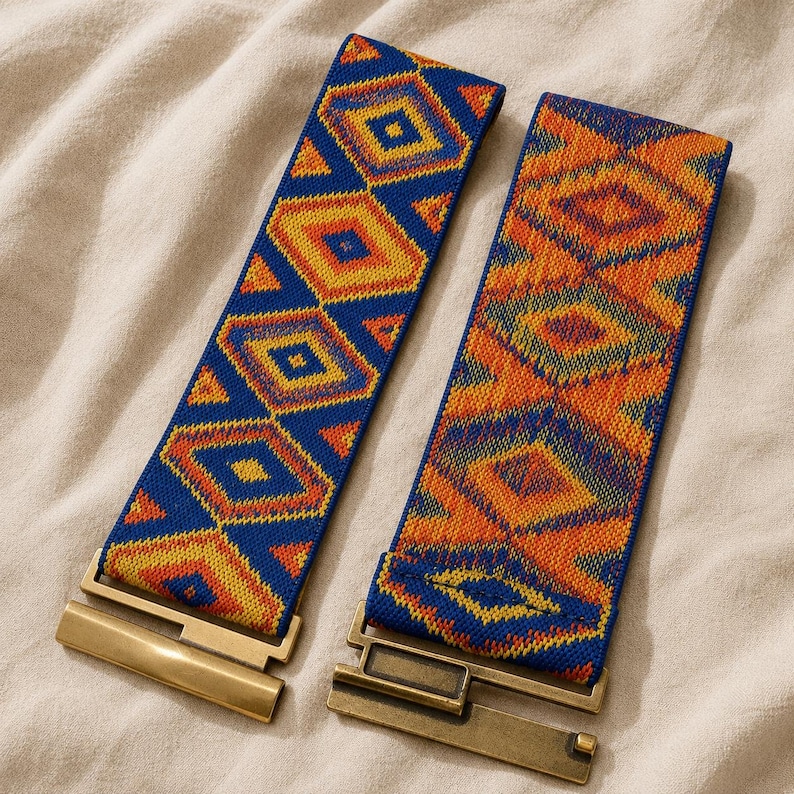 Puede incluir: Dos cinturones el&aacute;sticos con patrones geom&eacute;tricos en azul, naranja y amarillo. Cada cintur&oacute;n tiene un cierre rectangular de metal dorado. Los cinturones est&aacute;n sobre una superficie de tela beige.