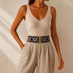 Puede incluir: Una camiseta sin mangas beige acanalada y pantalones de cintura alta se combinan con un cintur&oacute;n estampado. El cintur&oacute;n presenta un dise&ntilde;o geom&eacute;trico en negro, blanco y marr&oacute;n, con una hebilla rectangular dorada. El atuendo es de tonos neutros y elegante.