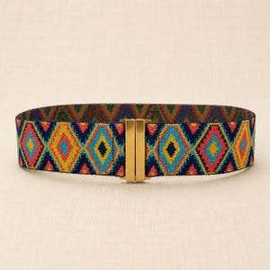 Puede incluir: Un cintur&oacute;n el&aacute;stico colorido con un patr&oacute;n geom&eacute;trico de diamantes en tonos de azul, rosa, amarillo y dorado. El cintur&oacute;n tiene un cierre de metal dorado. El cintur&oacute;n mide aproximadamente 5 cm de ancho.