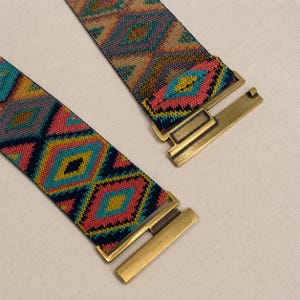 Puede incluir: Dos cinturones el&aacute;sticos coloridos con patrones geom&eacute;tricos en turquesa, rosa, amarillo y marr&oacute;n. Cada cintur&oacute;n tiene un cierre de metal dorado. Los cinturones se muestran sobre una superficie clara.