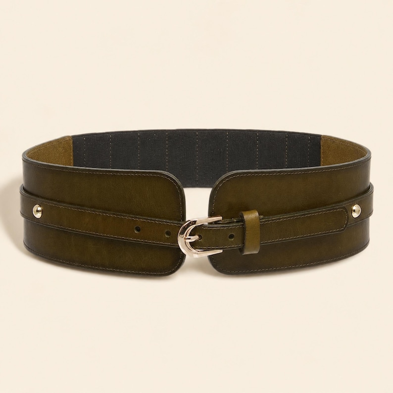 May include: A wide olive green waist belt featuring a smooth finish, a central silver-toned metal buckle, and two silver-toned metal studs on each side. The interior of the belt is lined with a dark grey fabric, and the strap includes multiple adjustment holes.