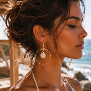 May include: A gold-toned hoop earring featuring a small, textured white seashell charm suspended from the center. The earring is attached to a gold-toned hook wire, creating a circular frame around the white shell, which has a detailed surface.