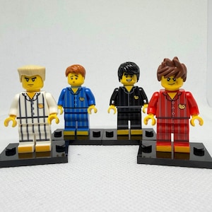 May include: Four Lego minifigures wearing pajamas. The pajamas are white with black stripes, blue with blue stripes, black with black stripes, and red with red stripes. Each figure has a different hairstyle and facial expression. They are standing on black Lego baseplates.