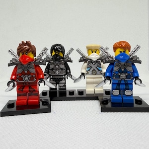 May include: Four Lego Ninjago minifigures in red, black, white, and blue outfits. Each figure has a matching head covering and a silver weapon. They stand on black baseplates.