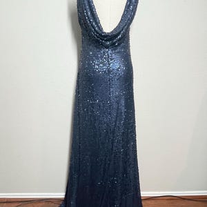 May include: A navy blue sequined gown with a cowl neckline. The sleeveless dress is floor-length and displayed on a mannequin. The dress is covered in small, reflective sequins.