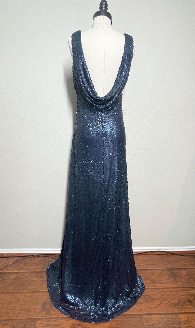May include: A navy blue sequined gown with a cowl neckline. The sleeveless dress is floor-length and displayed on a mannequin. The dress is covered in small, reflective sequins.