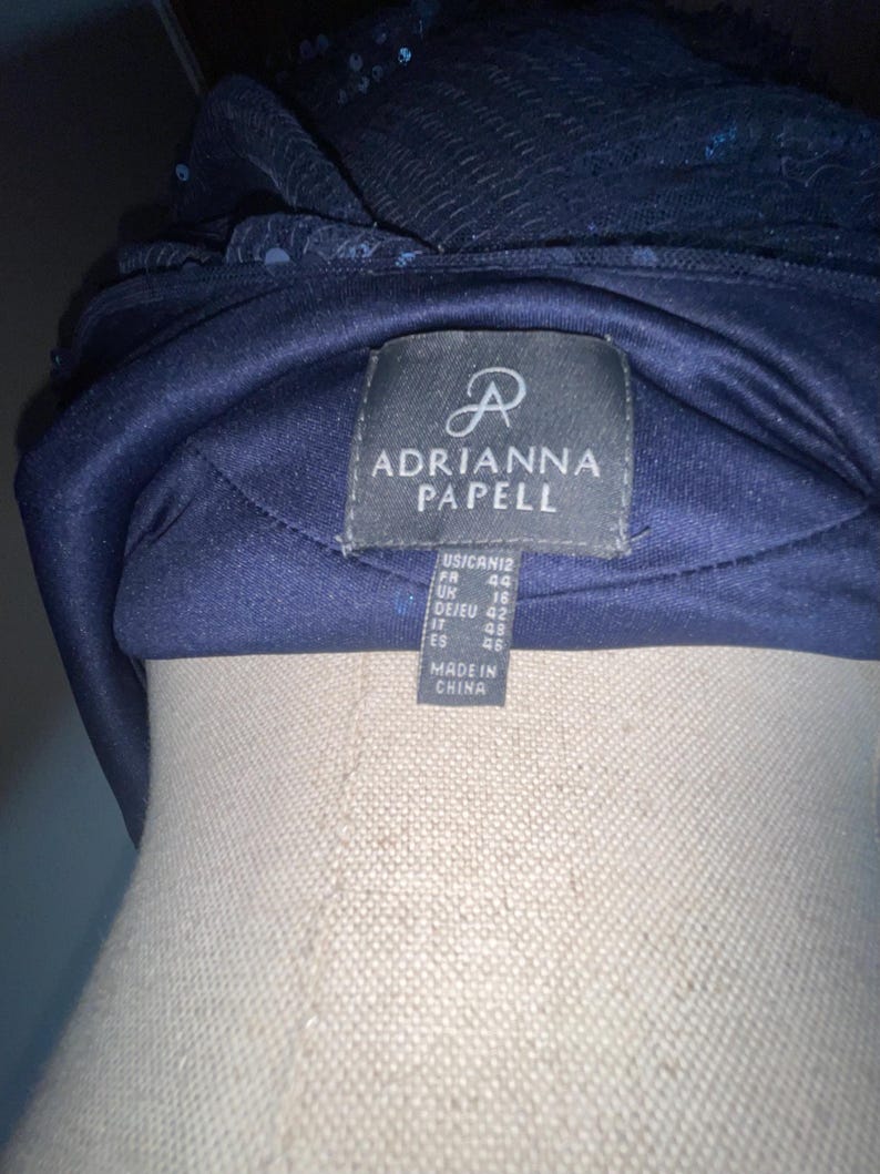 May include: A navy blue formal headpiece with sequin and fabric details. The label reads "ADRIANNA PAPELL" with size information. Made in China.
