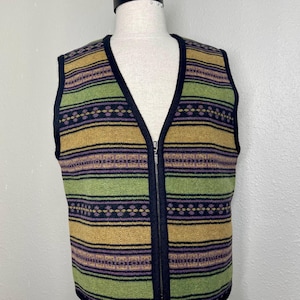 May include: A sleeveless vest featuring a horizontal striped pattern in shades of olive green, mustard yellow, and dark purple. The garment has a black trim along the V-neckline, armholes, and hem, and includes a central silver-toned metal zipper closure.
