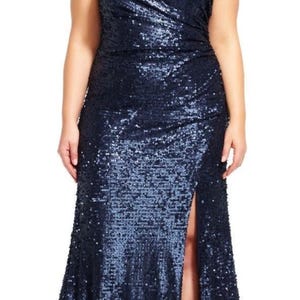 May include: A sleeveless, navy blue sequin gown with a high slit. The dress has a fitted bodice and a flowing skirt. The model is wearing black sandals. The dress is suitable for formal events.