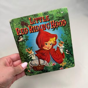 May include: Vintage children's book titled "Little Red Riding Hood." The cover features an illustration of a girl in a red hooded cloak, surrounded by green foliage and birds. The title is in red and yellow lettering.