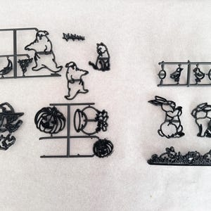 May include: A selection of black plastic cookie cutters in diverse shapes, such as ghosts, a witch on a broom, pumpkins, Easter bunnies, and chicks. The cutters are on a white surface, with a coin for scale.