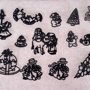 May include: A selection of black Christmas-themed cookie cutters in various shapes, including bells, snowmen, a Christmas tree, Santa Claus, and a nativity scene. Also included are a decorative stand and a few other shapes.