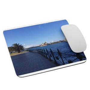 May include: A rectangular mousepad featuring a scenic view of Sydney Harbour, Australia, with the Opera House and water in the background. A white computer mouse rests on the pad. The mousepad has a white border.