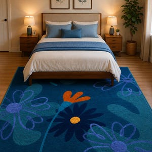 Puede incluir: Una alfombra rectangular con un fondo azul profundo y grandes patrones florales estilizados en tonos azul claro, azul oscuro y naranja. El diseño incluye motivos florales prominentes con centros circulares y pétalos curvos.
