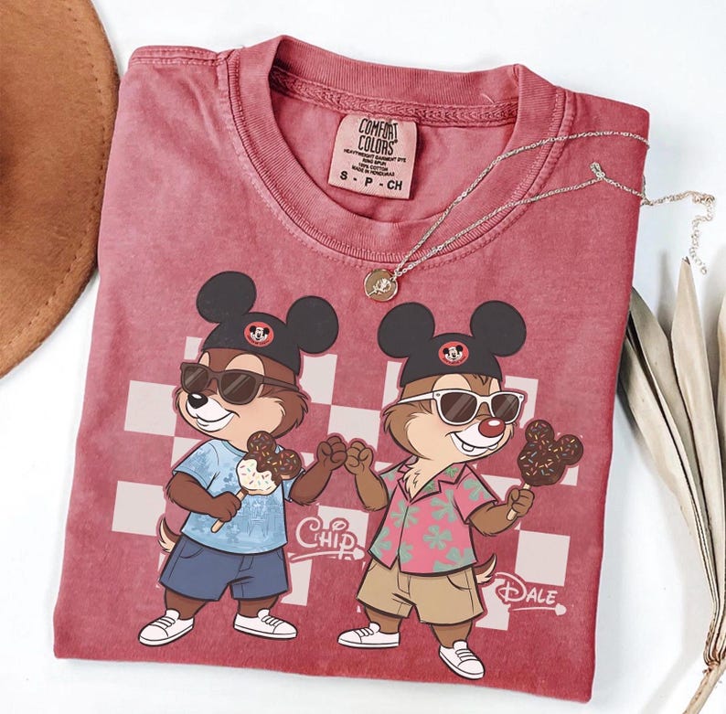 Peut inclure: T-shirt rouge Comfort Colors avec un motif de dessin anim&eacute; de Tic et Tac portant des lunettes de soleil et tenant des glaces. Le t-shirt a un fond &agrave; carreaux et les mots "Chip" et "Dale" sont imprim&eacute;s.