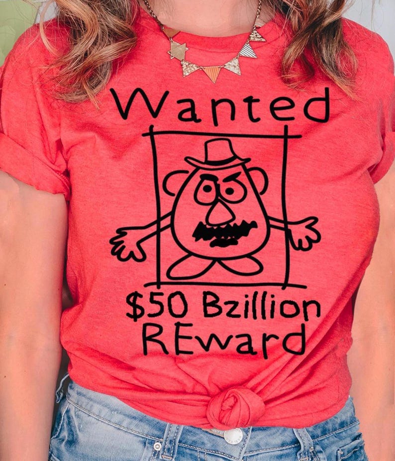 K&ouml;nnte beinhalten: Ein korallenfarbenes T-Shirt mit einer schwarz-wei&szlig;en Cartoon-Illustration eines kartoffelartigen Charakters in einem Fahndungsplakat. Der Text "Wanted" und "$50 Bzillion REWARD" sind ebenfalls in Schwarz dargestellt.