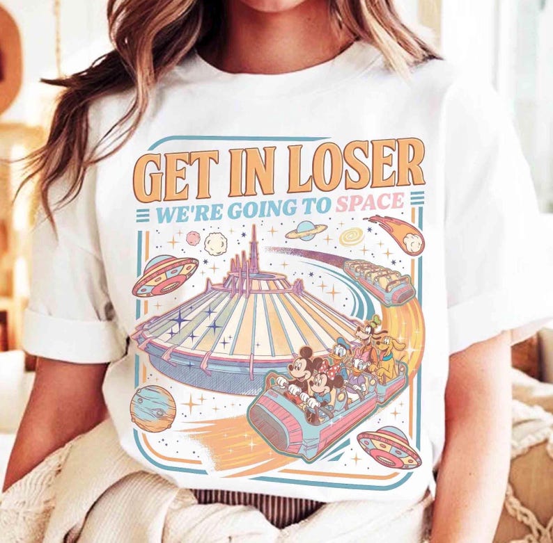 May include: White t-shirt with a colorful graphic featuring a space-themed design. The graphic includes the text "GET IN LOSER WE'RE GOING TO SPACE" above a roller coaster with Disney characters, planets, and UFOs. The design is in shades of orange, blue, and pink.