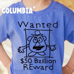 K&ouml;nnte beinhalten: Blaues T-Shirt mit dem Wort "Columbia" in wei&szlig;em Text oben. Das Shirt zeigt eine schwarz-wei&szlig;e Cartoon-Zeichnung eines Kartoffelkopf-Charakters in einem Fahndungsplakat mit dem Text "Wanted" und "50 Milliarden Belohnung".