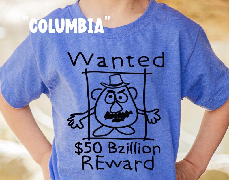 K&ouml;nnte beinhalten: Blaues T-Shirt mit dem Wort "Columbia" in wei&szlig;em Text oben. Das Shirt zeigt eine schwarz-wei&szlig;e Cartoon-Zeichnung eines Kartoffelkopf-Charakters in einem Fahndungsplakat mit dem Text "Wanted" und "50 Milliarden Belohnung".