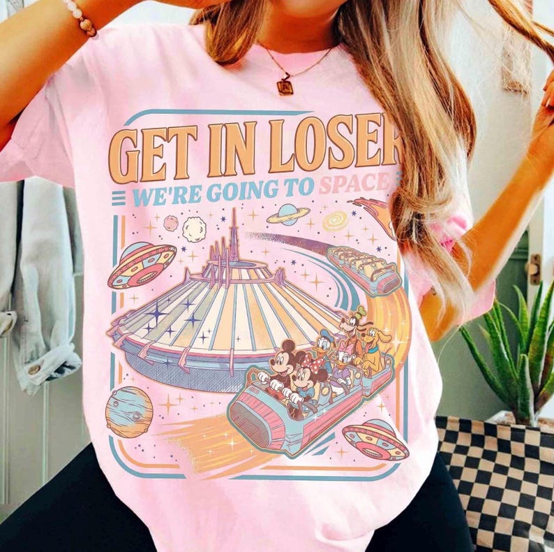 May include: Pink t-shirt with the text "GET IN LOSER WE'RE GOING TO SPACE" in orange and blue. The graphic features a space-themed amusement park ride with cartoon characters, planets, and flying saucers.