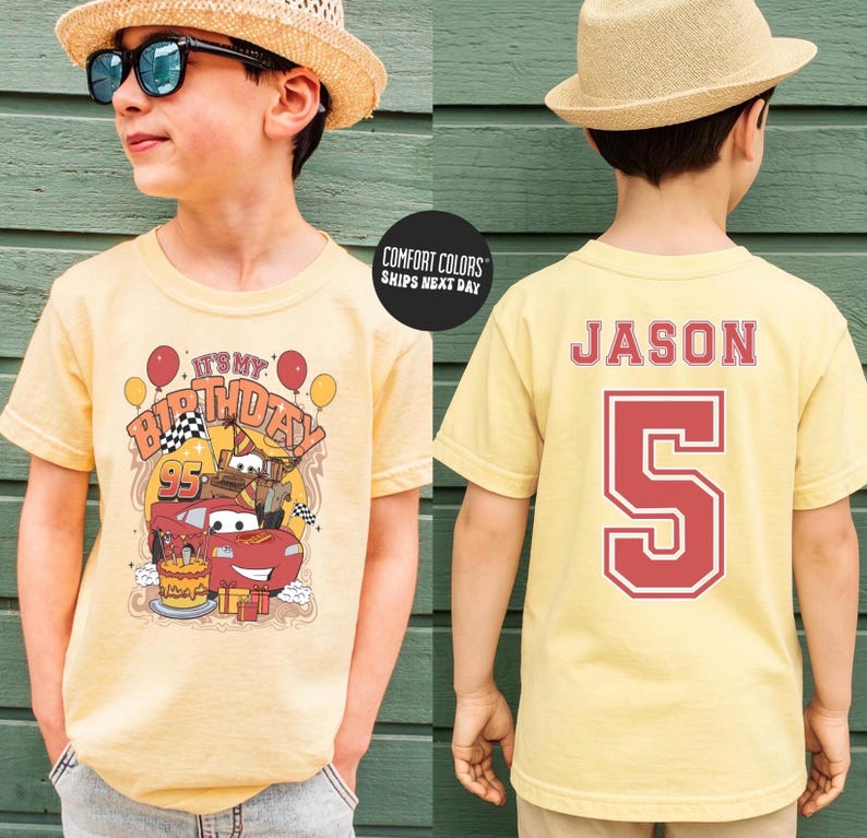 May include: A light yellow t-shirt featuring a birthday-themed graphic with the text "It's My Birthday" and a cartoon car design. The back of the shirt displays the name "Jason" and the number "5" in red.