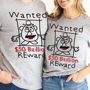 K&ouml;nnte beinhalten: Zwei graue T-Shirts mit einem Cartoon-Fahndungsplakat-Design. Das Plakat zeigt eine kartoffelartige Figur mit Hut, Schnurrbart und w&uuml;tenden Augen. Der Text "Wanted" und "$50 Bzillion REWARD" sind auf die Shirts gedruckt.