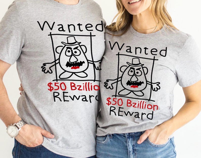 K&ouml;nnte beinhalten: Zwei graue T-Shirts mit einem Cartoon-Fahndungsplakat-Design. Das Plakat zeigt eine kartoffelartige Figur mit Hut, Schnurrbart und w&uuml;tenden Augen. Der Text "Wanted" und "$50 Bzillion REWARD" sind auf die Shirts gedruckt.