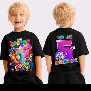 May include: Black t-shirt with a vibrant graphic of video game characters and the name "Kaiden". The back of the shirt says "It's My Super 5th Birthday". The design is in bright colours. The t-shirt is for a child.
