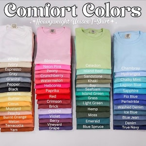 May include: A selection of folded Comfort Colors unisex t-shirts in a variety of colours. The image showcases a spectrum of shades, including white, pink, green, and blue. Each stack of shirts is labelled with its colour name, such as "Blossom" and "Chambray."