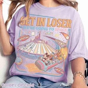 May include: Orchid-colored t-shirt with a retro-style graphic. The design features the text "GET IN LOSER WE'RE GOING TO SPACE" above a depiction of a space-themed amusement park ride with cartoon characters and flying saucers.