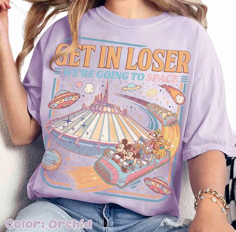 May include: Orchid-colored t-shirt with a retro-style graphic. The design features the text "GET IN LOSER WE'RE GOING TO SPACE" above a depiction of a space-themed amusement park ride with cartoon characters and flying saucers.