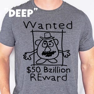 K&ouml;nnte beinhalten: Graues T-Shirt mit einer schwarzen Cartoon-Illustration eines kartoffelartigen Charakters in einem Fahndungsplakat. Der Text auf dem Shirt lautet "DEEP", "Wanted", "$50 Bzillion REWARD".
