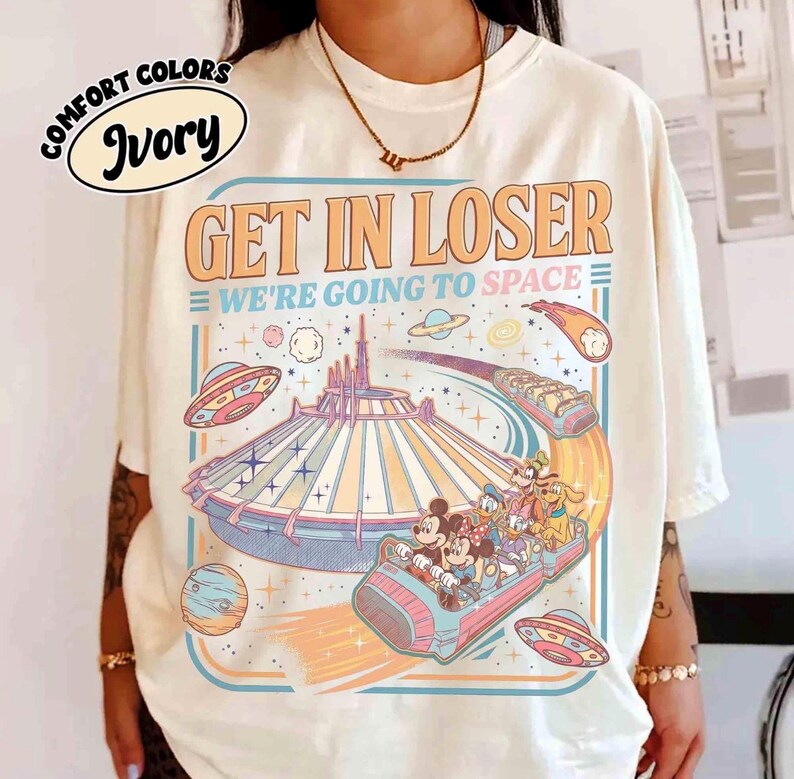 May include: Ivory-colored t-shirt with the text "GET IN LOSER WE'RE GOING TO SPACE" and a graphic of a space-themed amusement park ride. The graphic includes cartoon characters and planets.