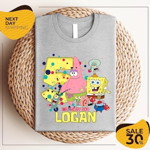 Op de afbeelding: Een grijs t-shirt met een kleurrijk cartoonontwerp met personages uit SpongeBob SquarePants. Het ontwerp bevat SpongeBob, Patrick Star en andere personages, met de tekst "BIRTHDAY BOY LOGAN" in het geel.
