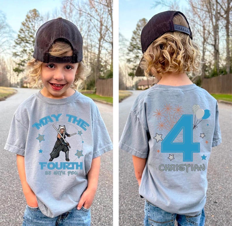 May include: A light blue t-shirt featuring the text "MAY THE FOURTH BE WITH YOU" and a character graphic with lightsabers. The back of the shirt displays a large number 4, fireworks, balloons, stars, and the name "CHRISTIAN".