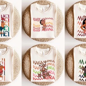May include: Six cream-colored t-shirts with colorful graphics from the animated movie Moana. The shirts feature characters Hei Hei, Baby Moana, Moana, Tui, Kakamora, and Maui, with their names printed in various fonts.