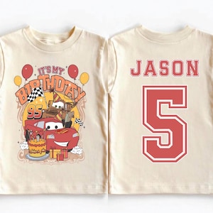 May include: A cream-colored t-shirt featuring a birthday design with the text "It's My Birthday" and the number "95". The design includes cartoon cars, balloons, and a birthday cake. The back of the shirt displays the name "JASON" and the number "5" in red.