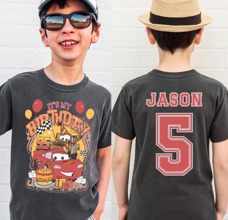 May include: Charcoal gray t-shirt with a colorful graphic featuring a red race car, birthday cake, and the text "IT'S MY BIRTHDAY". The back of the shirt displays the name "JASON" and the number "5" in red.