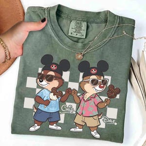 Peut inclure: T-shirt vert Comfort Colors avec des personnages de dessins anim&eacute;s Chip et Dale portant des lunettes de soleil et tenant des glaces. Le t-shirt a un motif &agrave; carreaux et les mots "Chip" et "Dale" sont imprim&eacute;s.