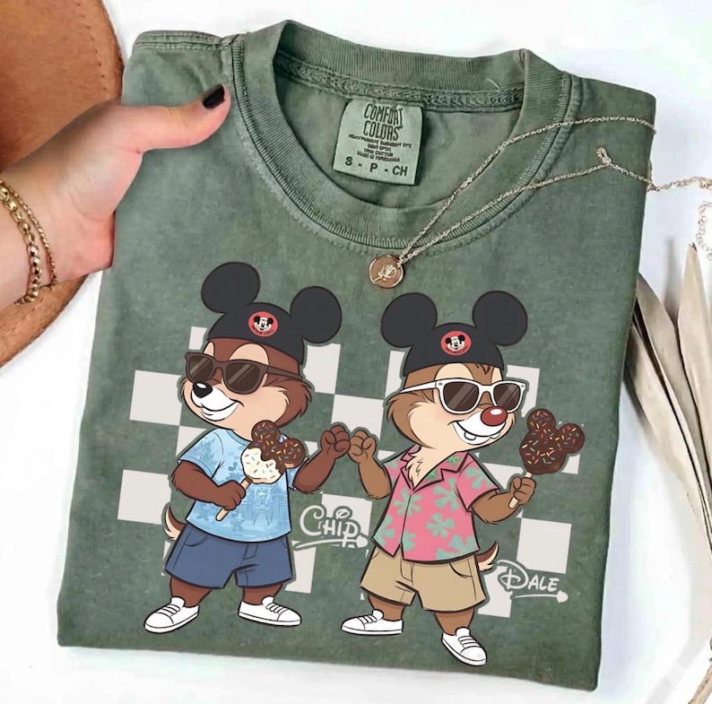 Peut inclure: T-shirt vert Comfort Colors avec des personnages de dessins anim&eacute;s Chip et Dale portant des lunettes de soleil et tenant des glaces. Le t-shirt a un motif &agrave; carreaux et les mots "Chip" et "Dale" sont imprim&eacute;s.