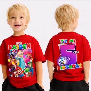 May include: Red t-shirt with a colourful graphic of video game characters and the name "Kaiden" in white. The back of the shirt says "It's My 5th Birthday" in colourful text. The shirt is short-sleeved.