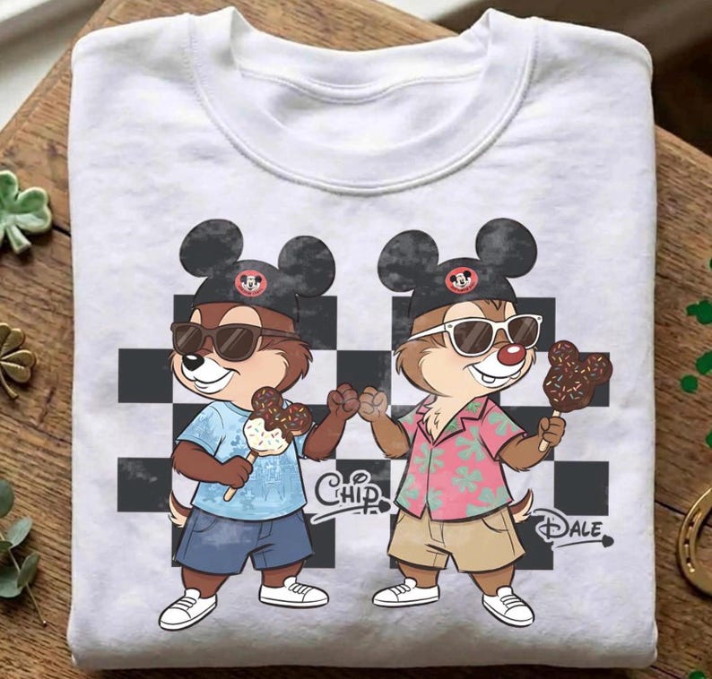Peut inclure: Sweat-shirt blanc &agrave; col rond avec une illustration de dessin anim&eacute; de Tic et Tac portant des lunettes de soleil et des chapeaux de Mickey Mouse. Ils tiennent des glaces enrob&eacute;es de chocolat. Les mots "Chip" et "Dale" sont imprim&eacute;s.