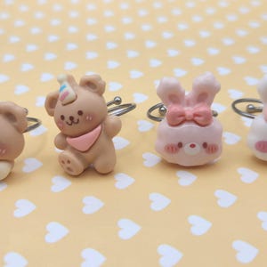 May include: Four adjustable rings featuring miniature sculpted animal figures. Two rings display brown bears with party hats and bows, while the other two feature pink and white rabbits with bows. Each figure has a small, detailed face with rosy cheeks.