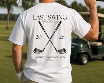 Peut inclure: Un t-shirt blanc avec un motif noir au dos représentant deux clubs de golf croisés. Le texte indique LAST SWING before the ring, 20 26, Andrew's Bachelor Party et Phoenix, AZ. Le motif est centré sur le dos du vêtement.