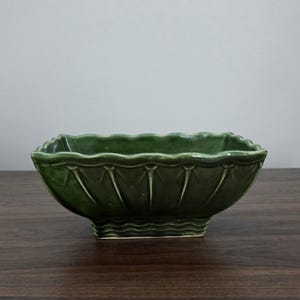 May include: A rectangular ceramic planter with a glossy dark green glaze. The exterior features a scalloped top edge, vertical ribbing along the sides, and a base with horizontal wavy lines, creating a textured appearance throughout the piece.