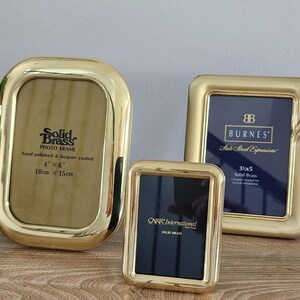 May include: Three polished solid brass photo frames of varying sizes. The largest oval frame is labeled 4 inches by 6 inches. The medium rectangular frame is labeled 3.5 inches by 5 inches. The smallest rectangular frame is labeled Carr International.