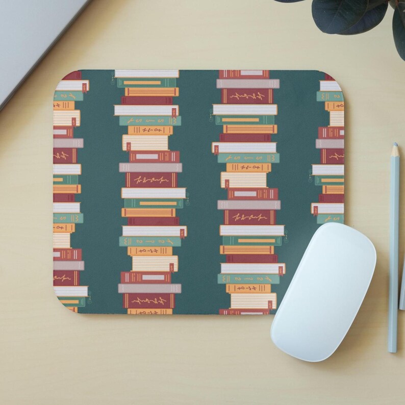 Puede incluir: Alfombrilla de rat&oacute;n rectangular con fondo verde azulado que presenta un patr&oacute;n repetido de libros apilados en varios colores. Los libros tienen una est&eacute;tica vintage, con texto visible en los lomos. Un rat&oacute;n de ordenador blanco descansa a la derecha.